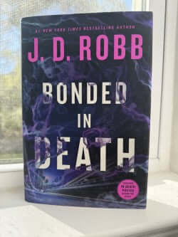Book titled 'Bonded in Death' by J.D. Robb on a surface with a window in the background