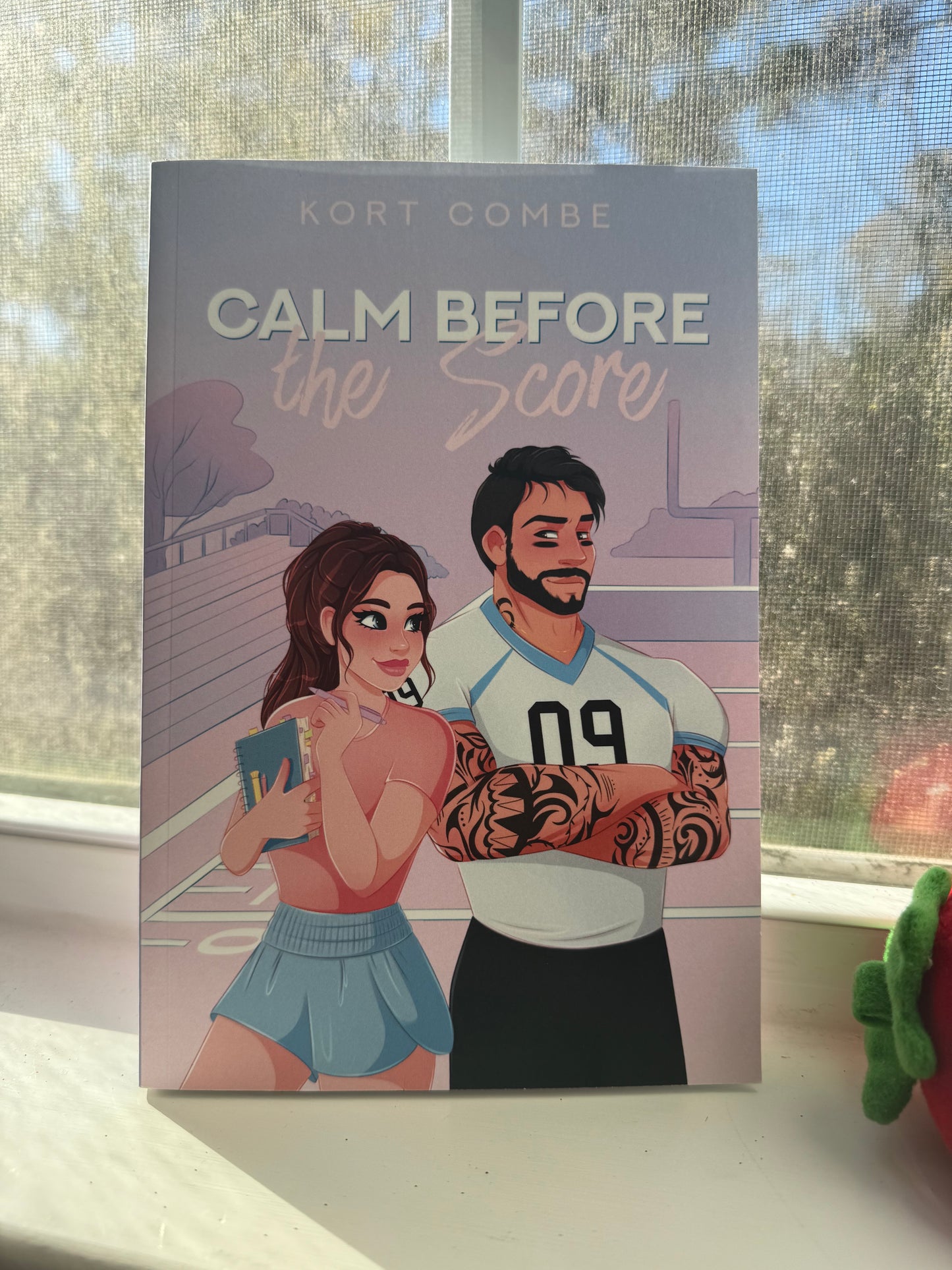 The image shows a book cover with a cartoon illustration of a man and a woman, presumably the main characters from the book 'Calm Before the Score' by Kort Combe.