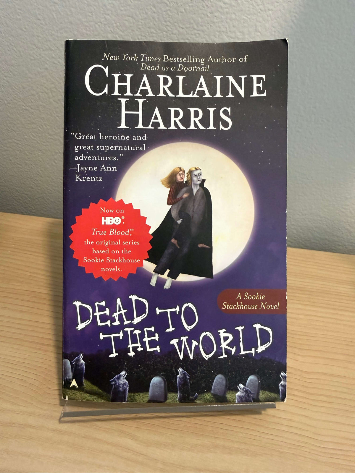 The book 'Dead to the World' by Charlaine Harris, a Solitude series novel, shown flat on a light-colored wooden surface next to a gray wall.