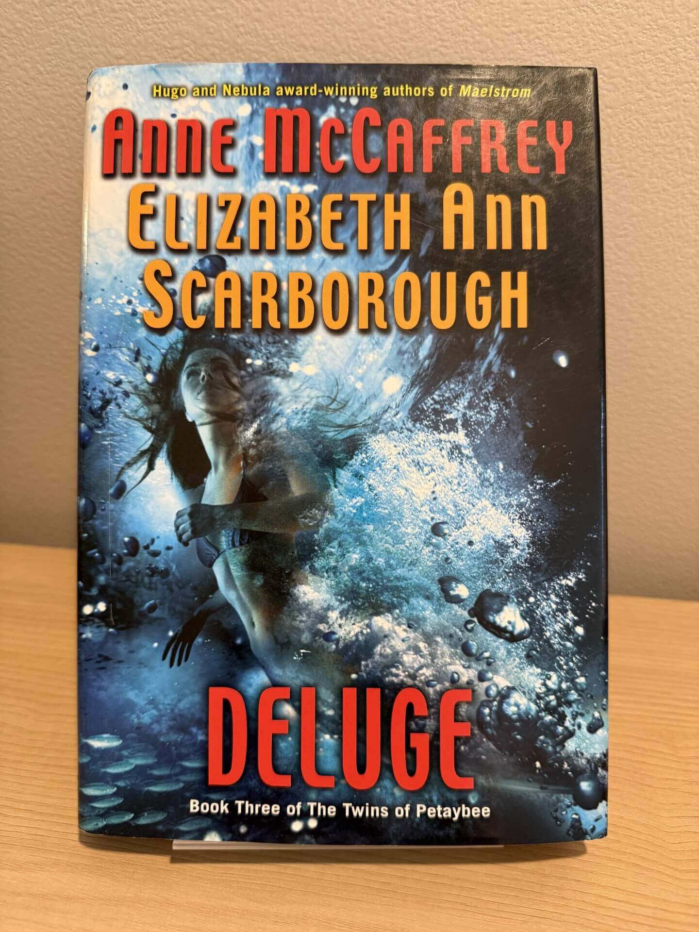 Book cover of 'Deluge' by Anne McCaffrey and Elizabeth Ann Scarborough on a wooden surface.