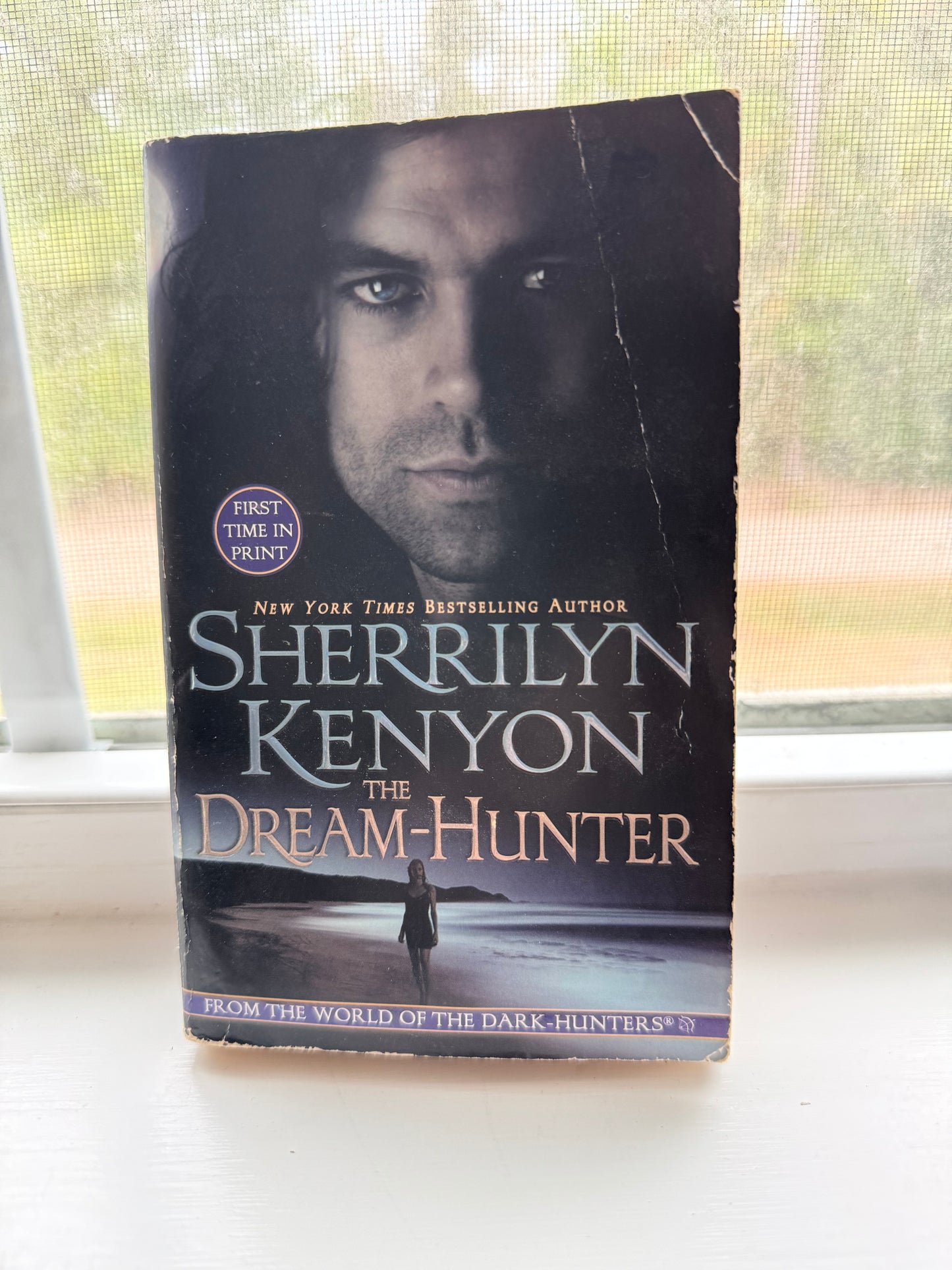 Book titled 'The Dream-Hunter' by Sherrilyn Kenyon on a surface with a window in the background