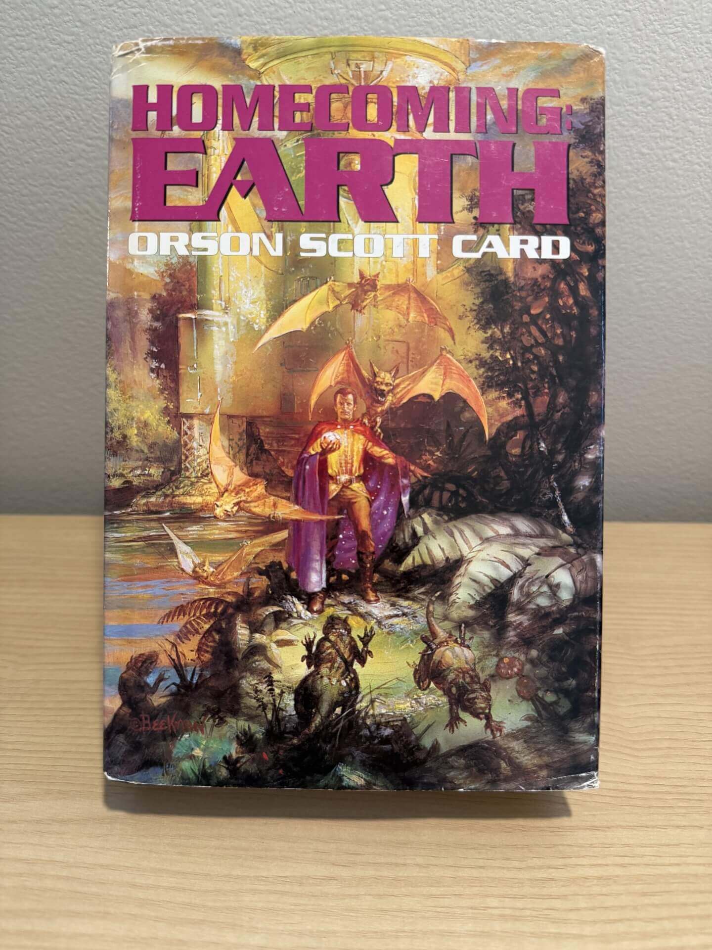 Book titled 'Homecoming Earth' by Orson Scott Card on a wooden surface with a gray background