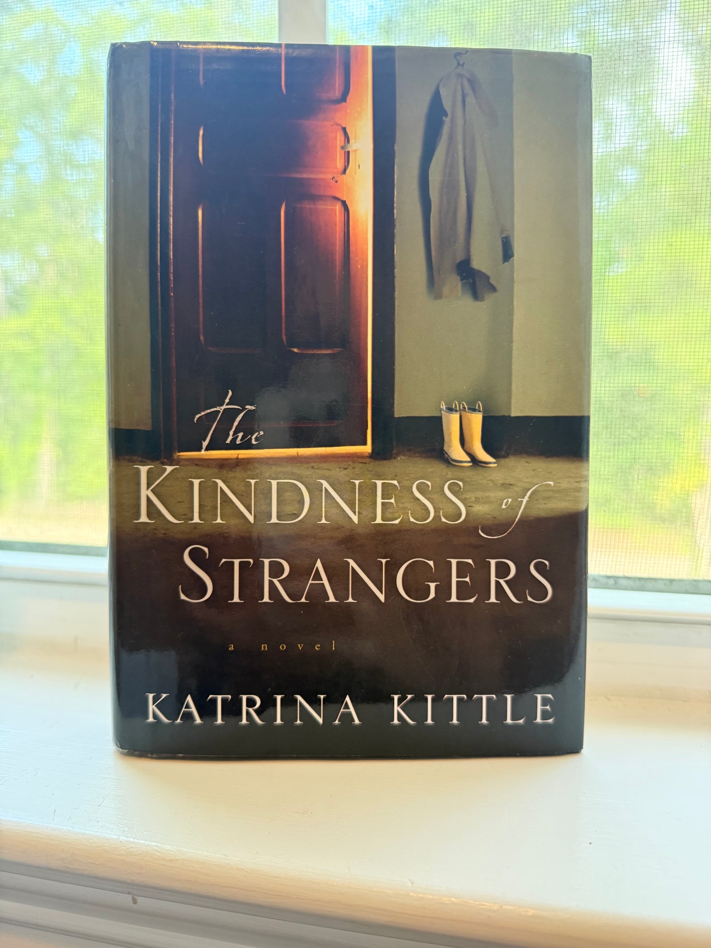 Book titled 'The Kindness of Strangers' by Katrina Kittle on a reflective surface with a blurred background