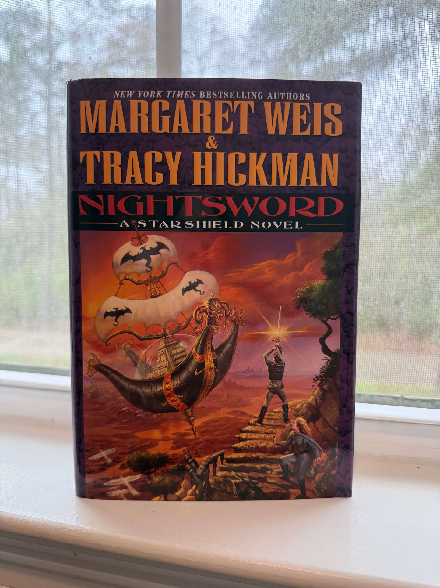 Book titled 'Nightsword' by Margaret Weis and Tracy Hickman on a windowsill.