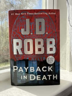 Book titled 'Payback in Death' by J.D. Robb on a windowsill.