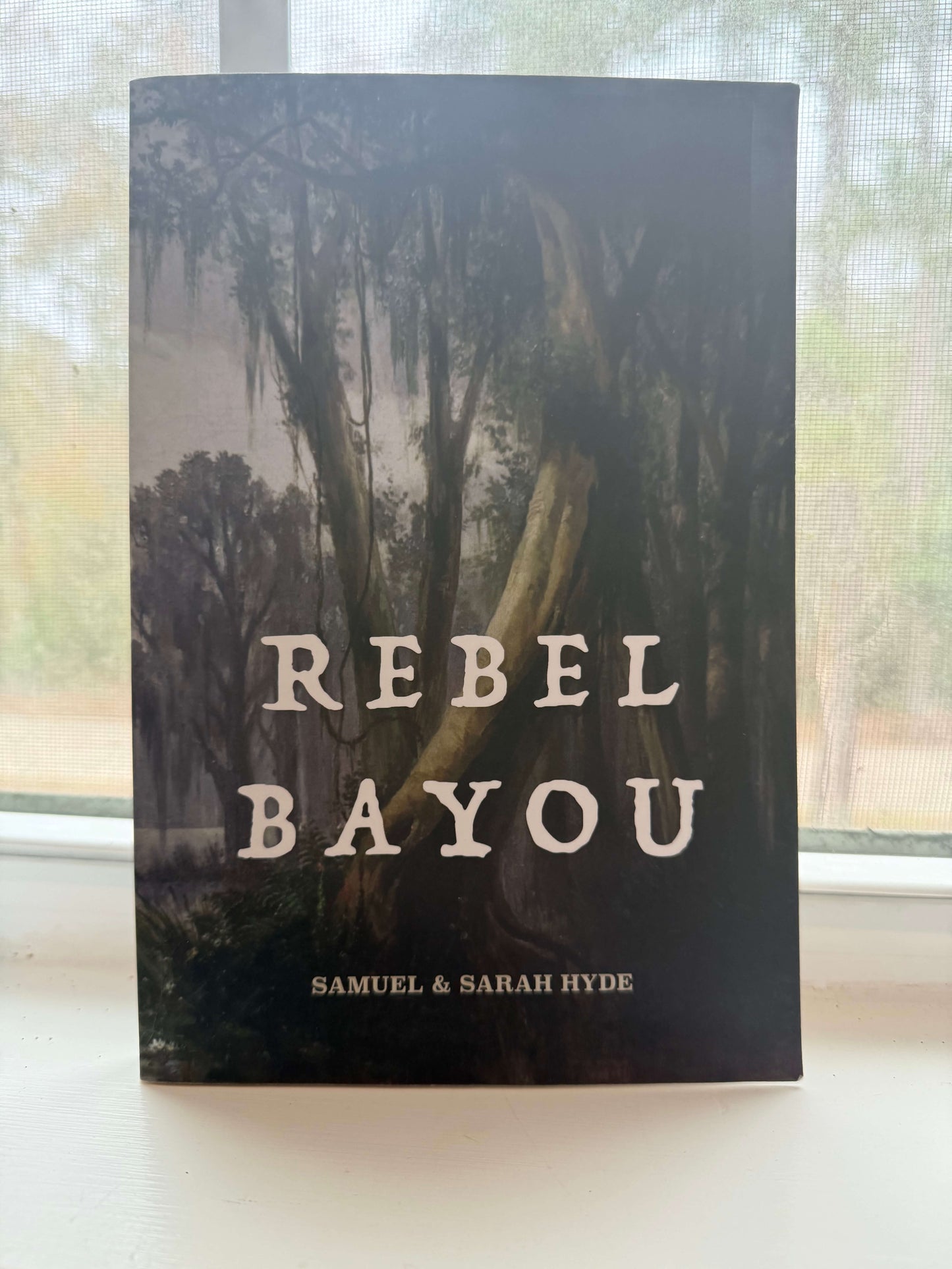 Book titled 'Rebel Bayou' by Samuel & Sarah Hyde with a forest cover on a blurred background.
