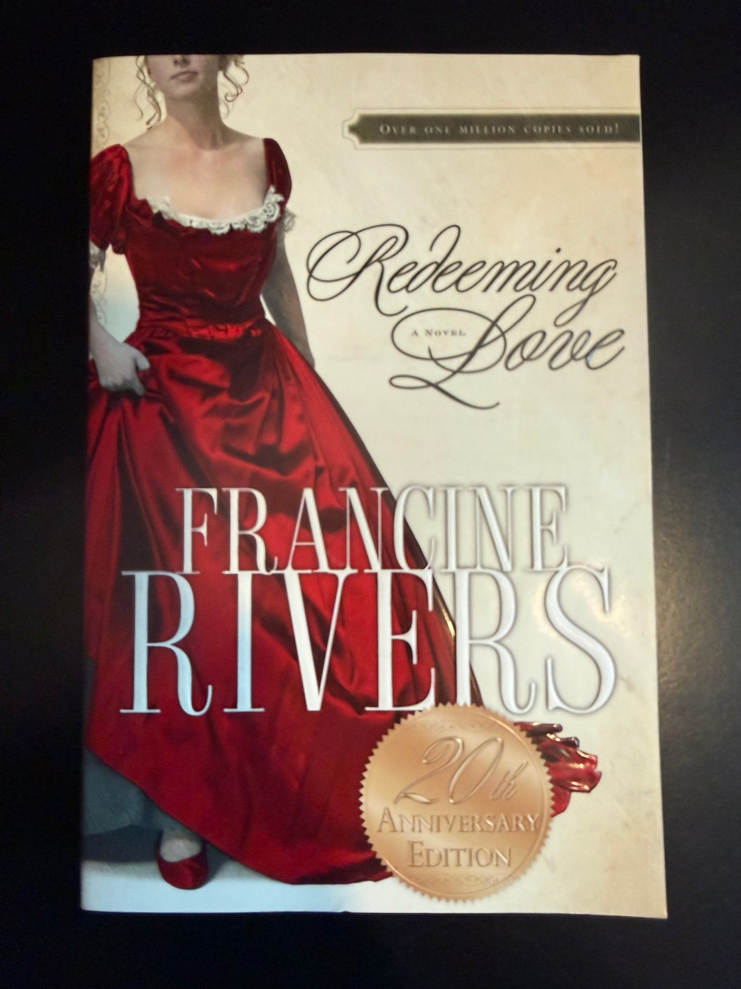 Book cover of 'Redeeming Love' by Francine Rivers with a woman in a red dress on a beige background.