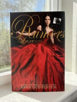 Book titled 'Rumors' by Anna Godbersen on a windowsill with a blurred background