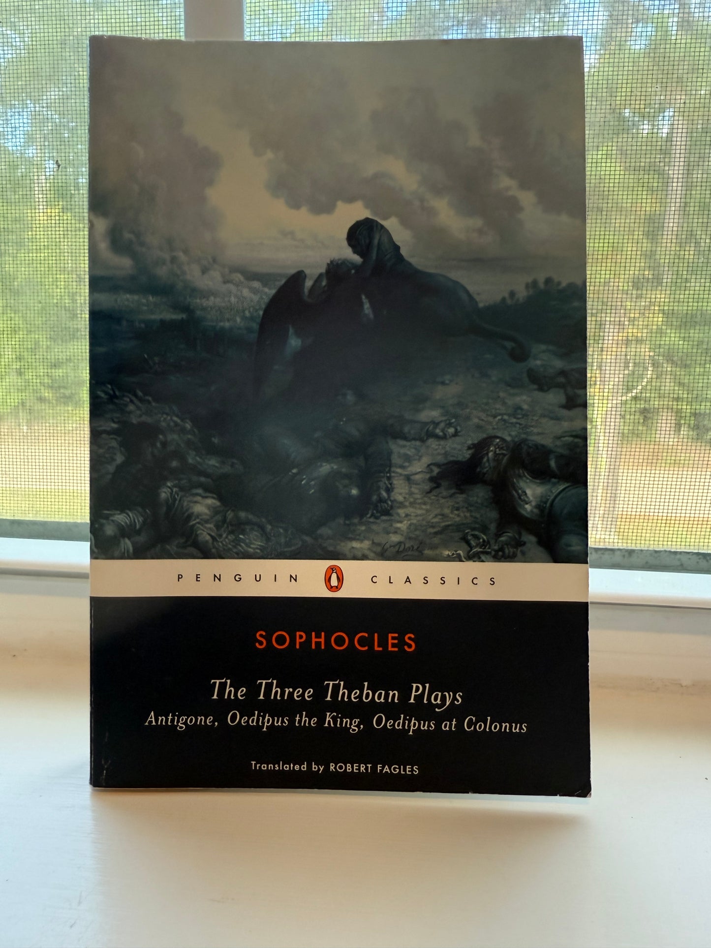 Book titled 'The Three Theban Plays' by Sophocles on a surface with a window in the background.