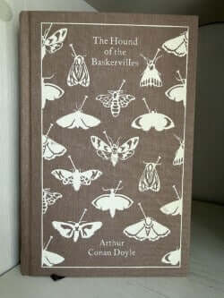 Book titled 'The Hound of the Baskervilles' with moth illustrations on a brown cover.