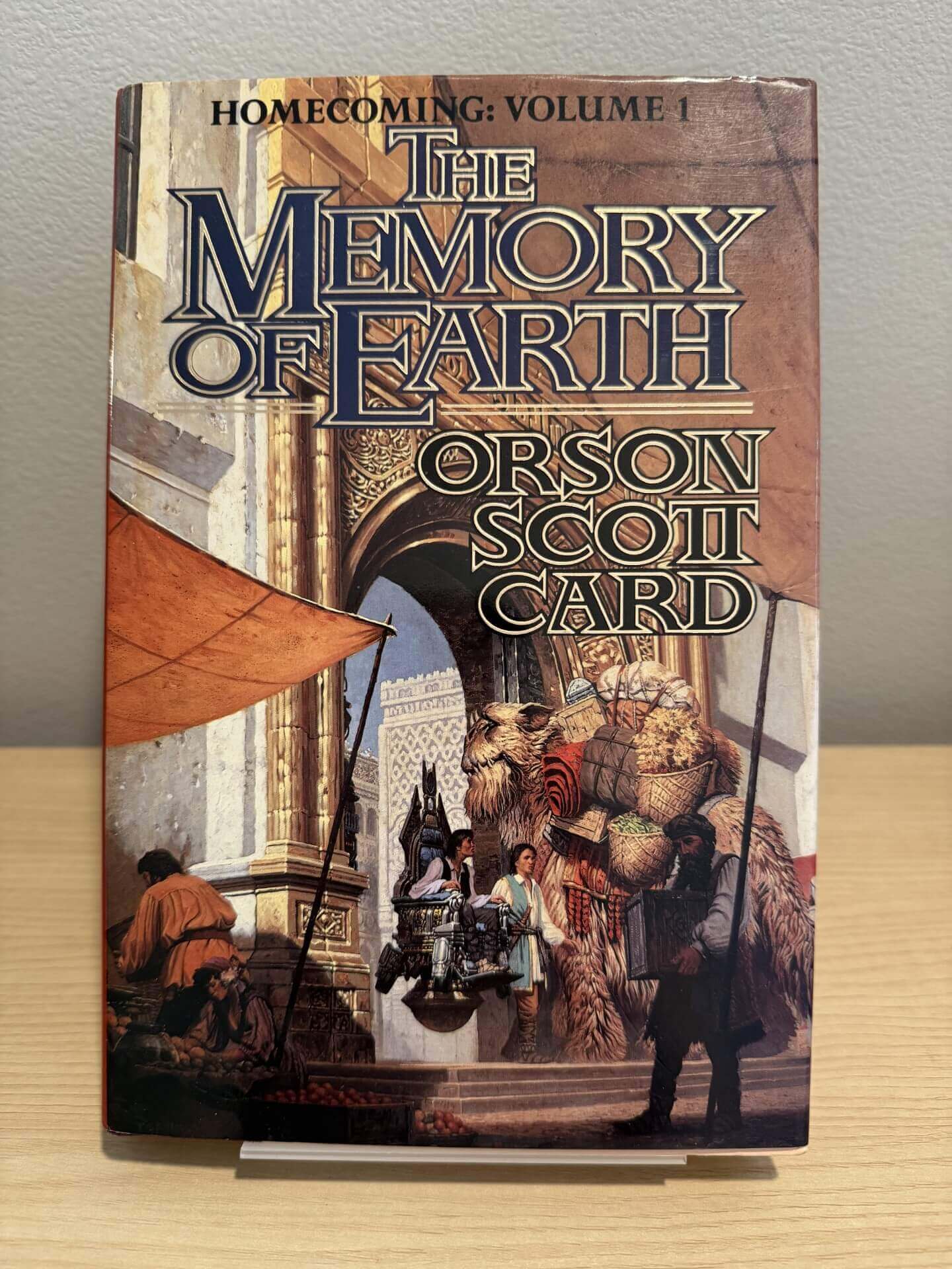 Book cover of 'The Memory of Earth' by Orson Scott Card on a wooden surface with a neutral background