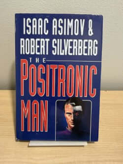 Book cover of The Positronic Man by Asimov and Silverberg on a wooden surface.