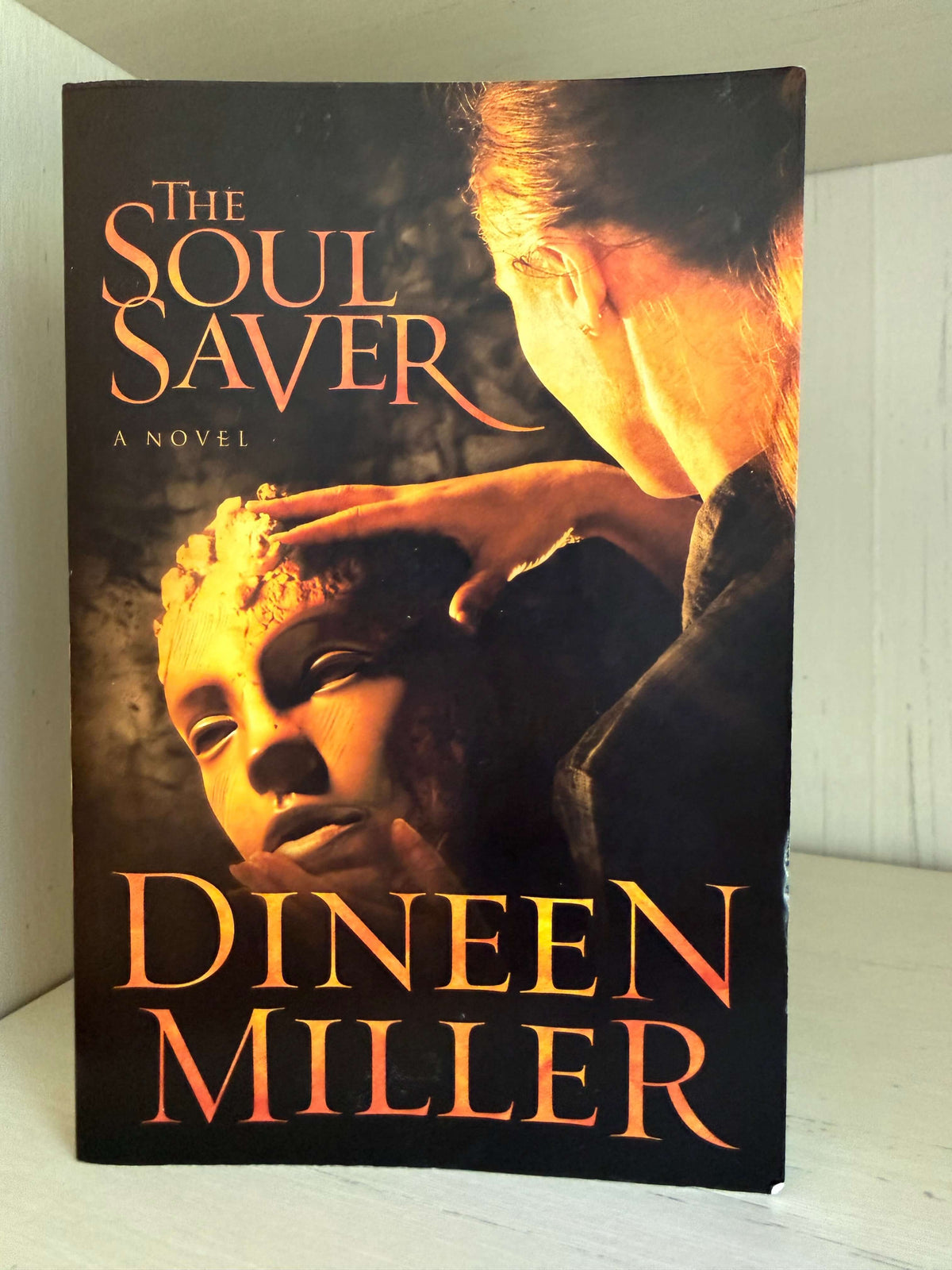 The book cover of 'The Soul Saver' by Dineen Miller, featuring a dramatic illustration of a woman touching a child's face, with the title and author name in orange lettering on a dark background.