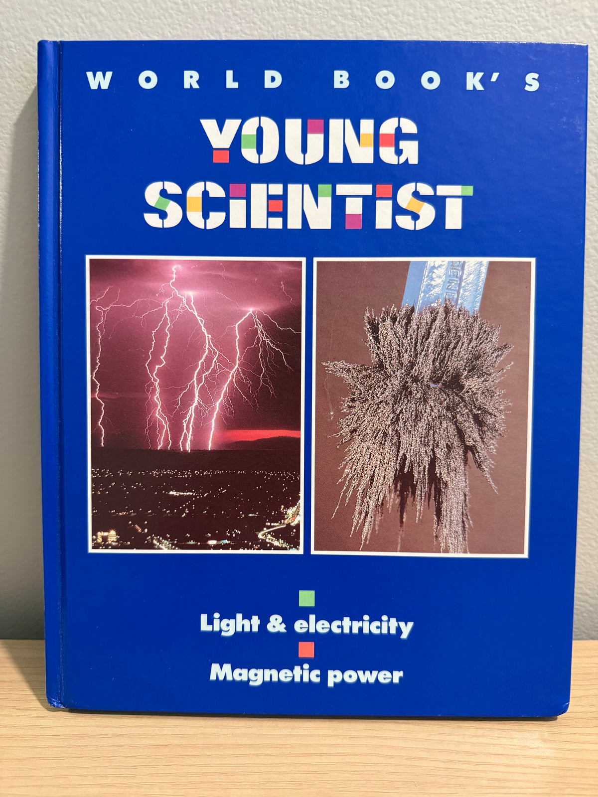 A hardcover book titled 'World Book's Young Scientist' with a bright blue cover, featuring two inset scientific photos and the text 'Light & electricity' and 'Magnetic power'.