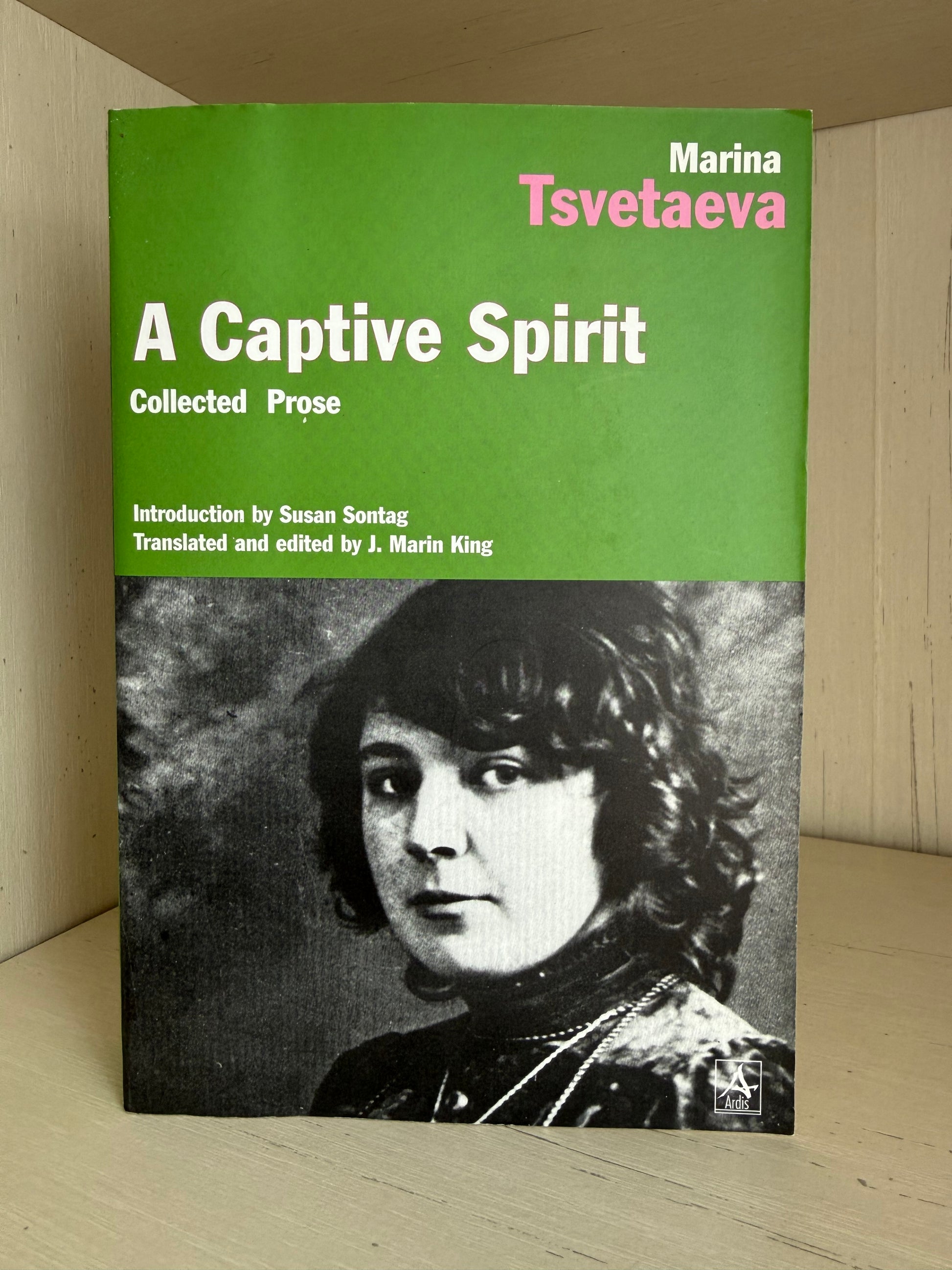 A book titled 'A Captive Spirit: Collected Prose' by Marina Tsvetaeva, featuring a green top half with white and pink text and a black-and-white portrait on the lower half, photographed standing on a light wood surface.
