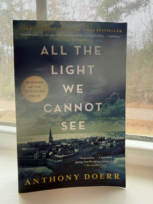 Book titled 'All the Light We Cannot See' by Anthony Doerr on a surface with a window in the background.