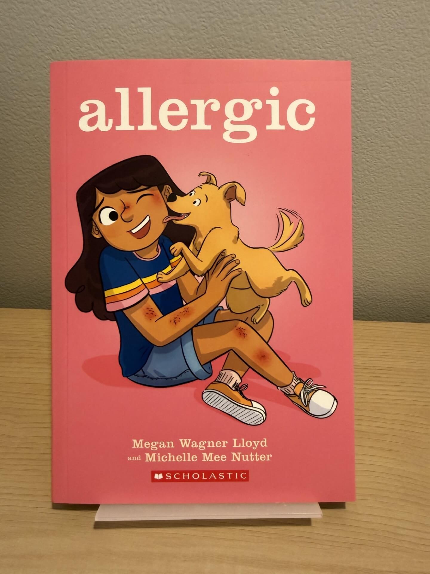 Book titled 'allergic' with a illustration of a girl holding a dog on a pink background