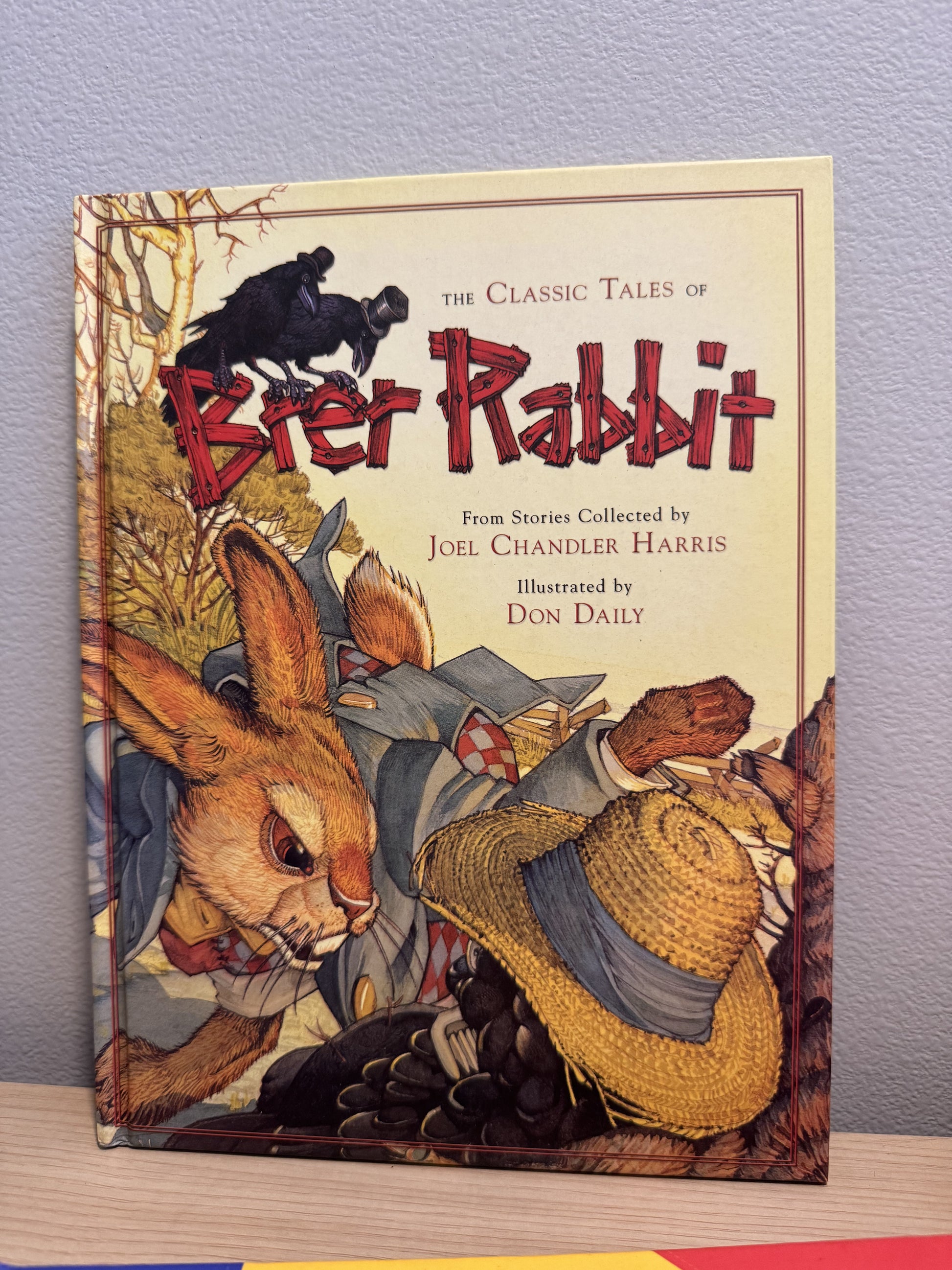 The Classic Tales of Brier Rabbit book by Don Daily, featuring vintage-style cover art of a rabbit, a crow, and a straw hat on a cream background, leaning against a gray wall on a wooden surface.