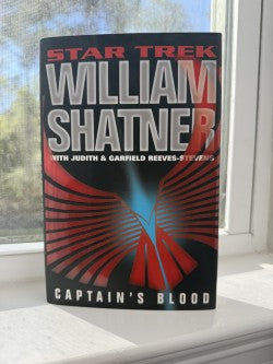 Book titled 'Captain's Blood' by William Shatner on a windowsill with a blurred outdoor background