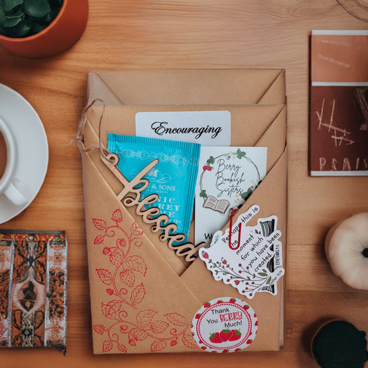 A subscription package containing a Christian-based non-fiction book or devotional, along with decorative items such as a card with the word 'Encouraging' and other small gifts, presented on a wooden table.