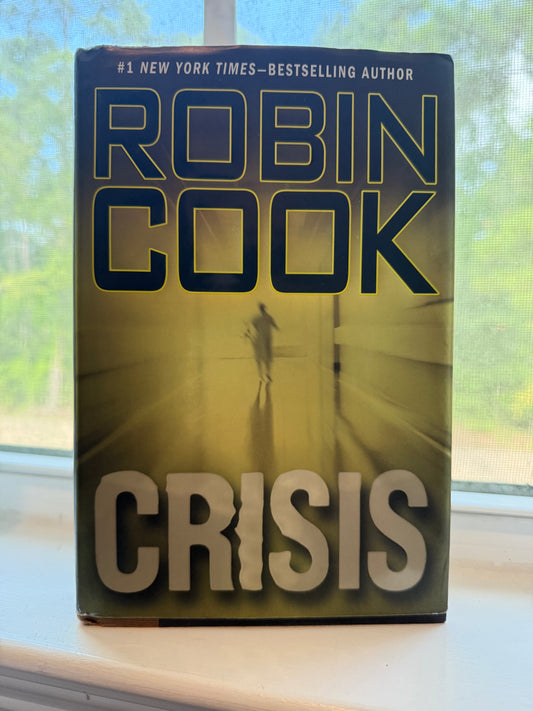 Book titled 'Crisis' by Robin Cook on a surface with a window in the background