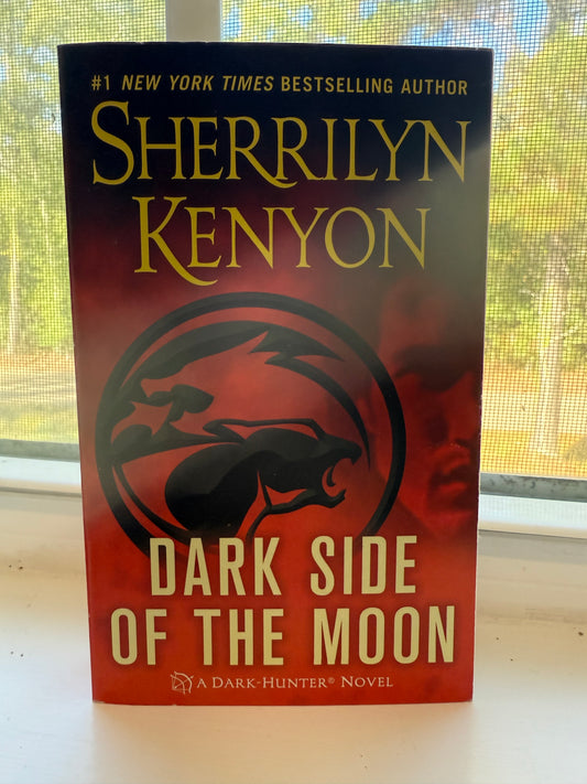 Book titled 'Dark Side of the Moon' by Sherrilyn Kenyon on a window pane.