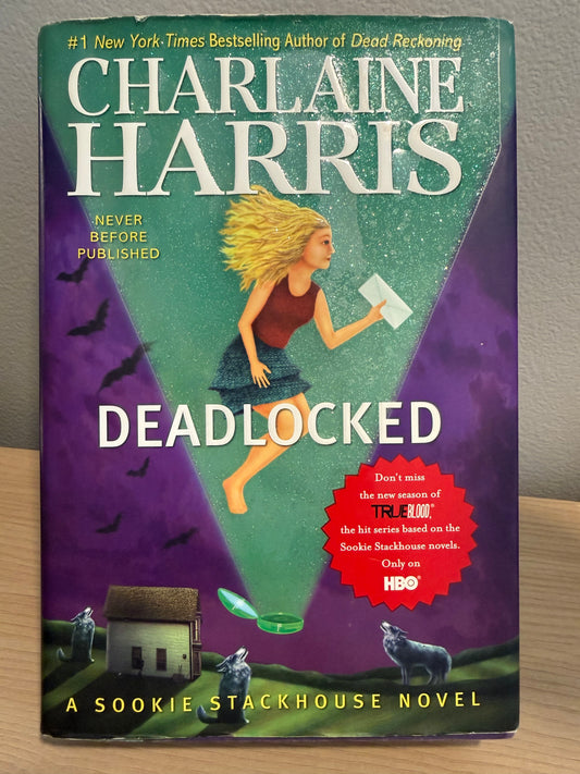 Book cover of the novel 'Deadlocked' by Charlaine Harris, featuring a purple and teal background with an illustration of a woman running, wolves, a small house, and a red circular promotional badge.