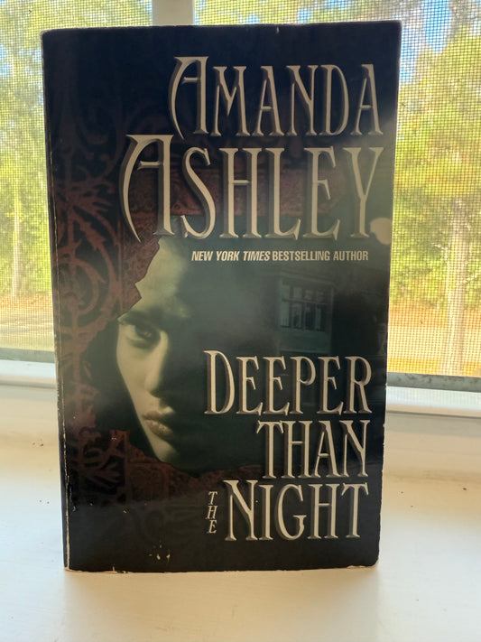 Book titled 'Deeper Than Night' by Amanda Ashley on a surface with a window in the background.