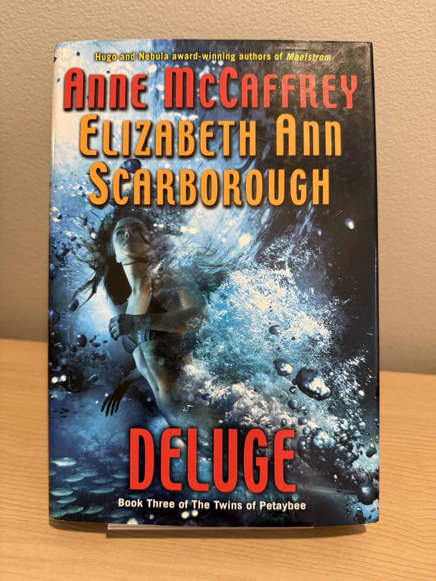 Book cover of 'Deluge' by Anne McCaffrey and Elizabeth Ann Scarborough on a wooden surface.