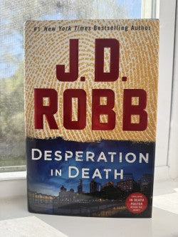 Book titled 'Desperation in Death' by J.D. Robb on a surface with a window in the background