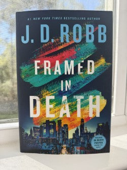 Book titled 'Framed in Death' by J.D. Robb with a colorful cover on a surface.
