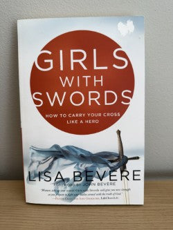 Book titled 'Girls with Swords' by Lisa Bevere on a wooden surface with a neutral background