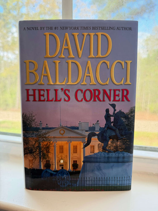 Book titled 'Hell's Corner' by David Baldacci on a windowsill with a blurred outdoor background.