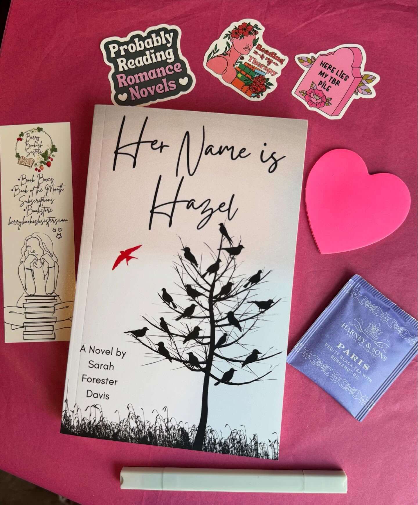 Book titled 'Her Name is Hazel' by Sarah Forester Davis on a pink surface with stickers and a heart.