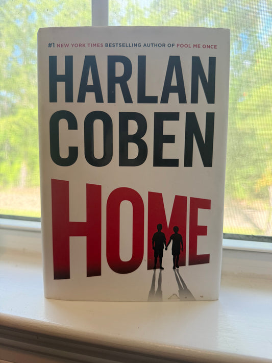 Book titled 'Home' by Harlan Coben on a surface with a window in the background