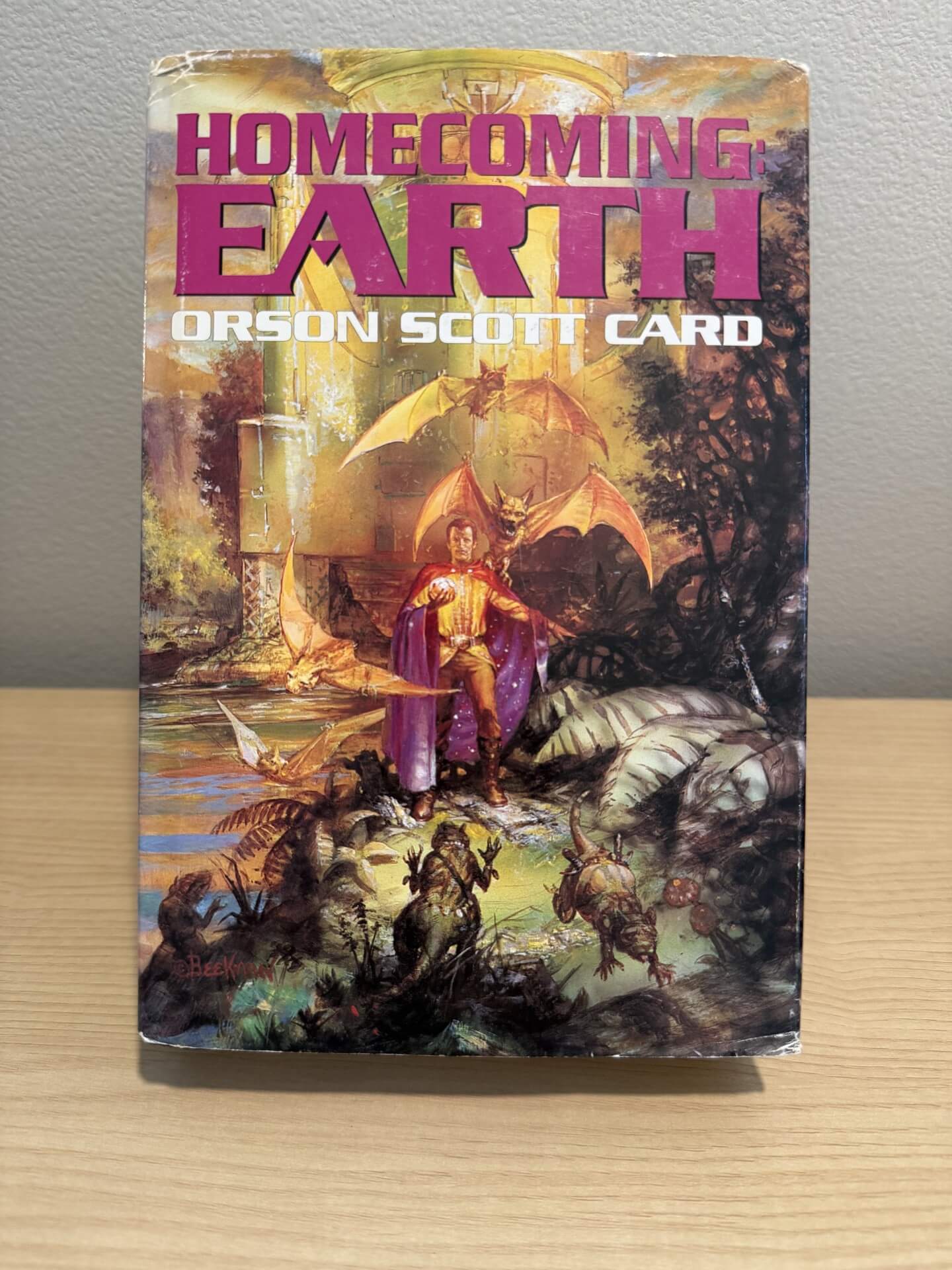 Book titled 'Homecoming Earth' by Orson Scott Card on a wooden surface with a gray background