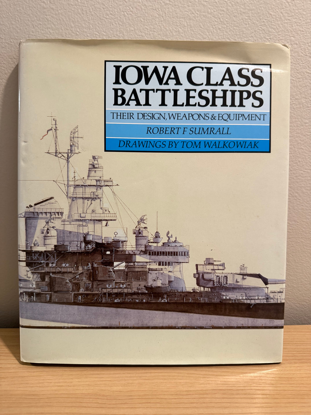 A book titled 'Iowa Class Battleships' by Robert F. Sumrall, with drawings by Tom Walkowiak, standing on a wooden surface against a beige wall.