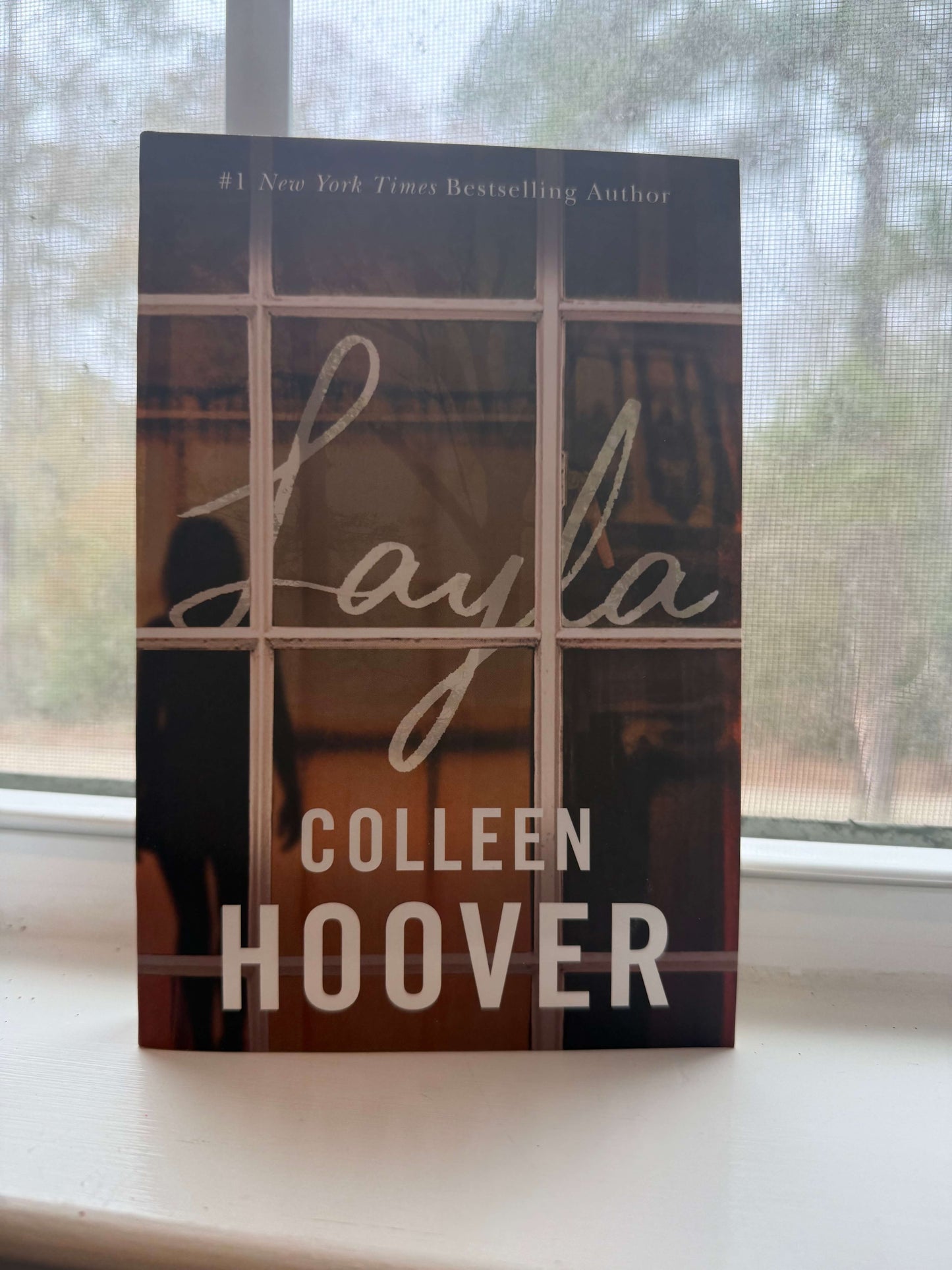 Book titled 'Layla' by Colleen Hoover on a windowsill with a blurred outdoor background