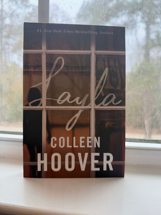 Book titled 'Layla' by Colleen Hoover on a windowsill with a blurred outdoor background