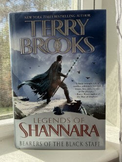 Book titled 'Legends of Shannara: Bearers of the Black Staff' by Terry Brooks on a white surface with a blurred background.
