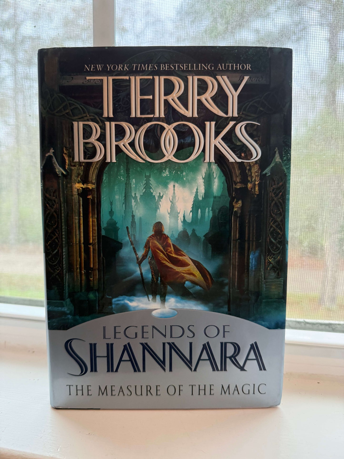 Book titled 'Legends of Shannara: The Measure of the Magic' by Terry Brooks on a surface with a window in the background.