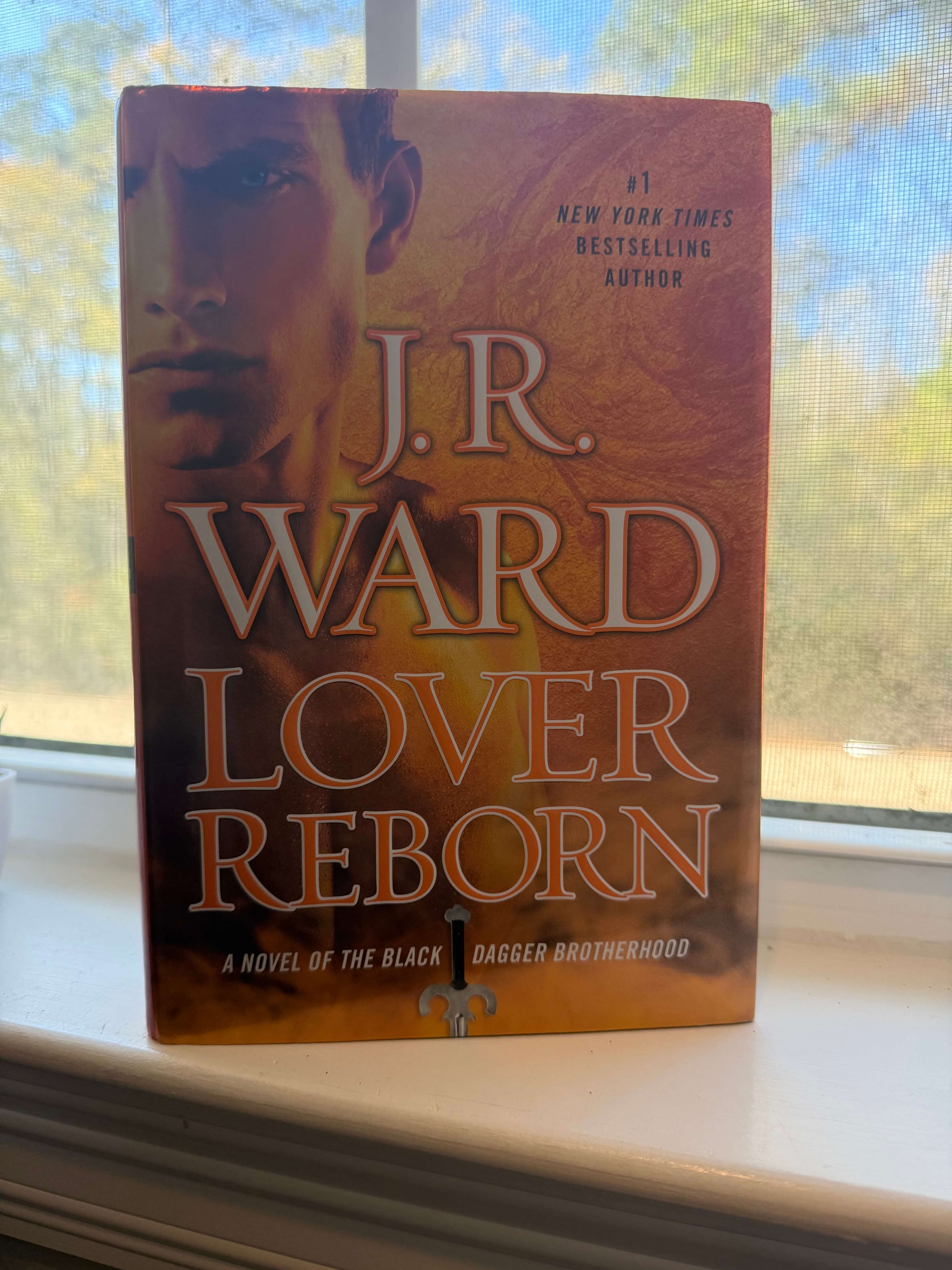 Book titled 'Lover Reborn' by J.R. Ward on a windowsill with a blurred outdoor background