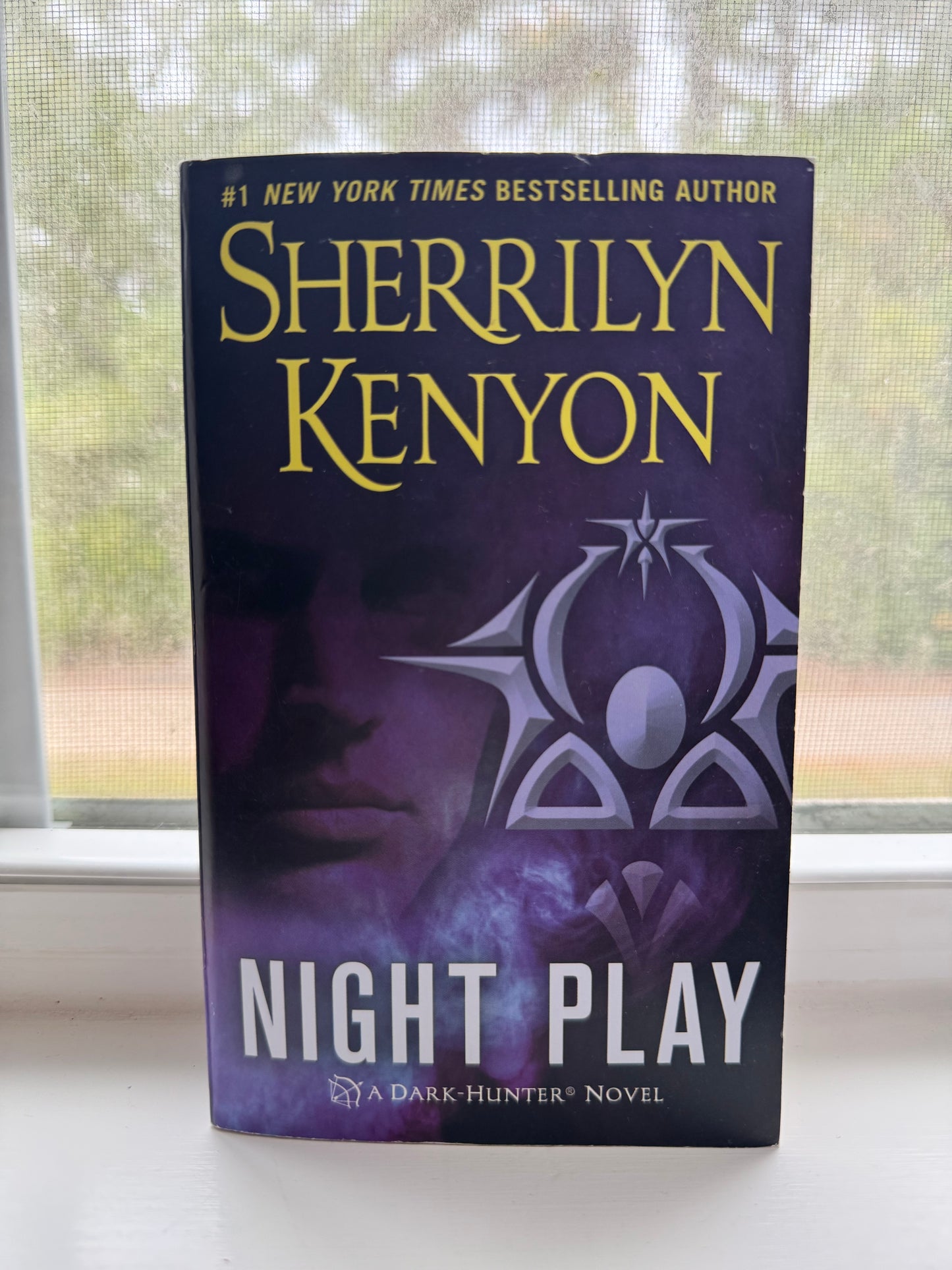 Book titled 'Night Play' by Sherrilyn Kenyon on a surface with a window in the background