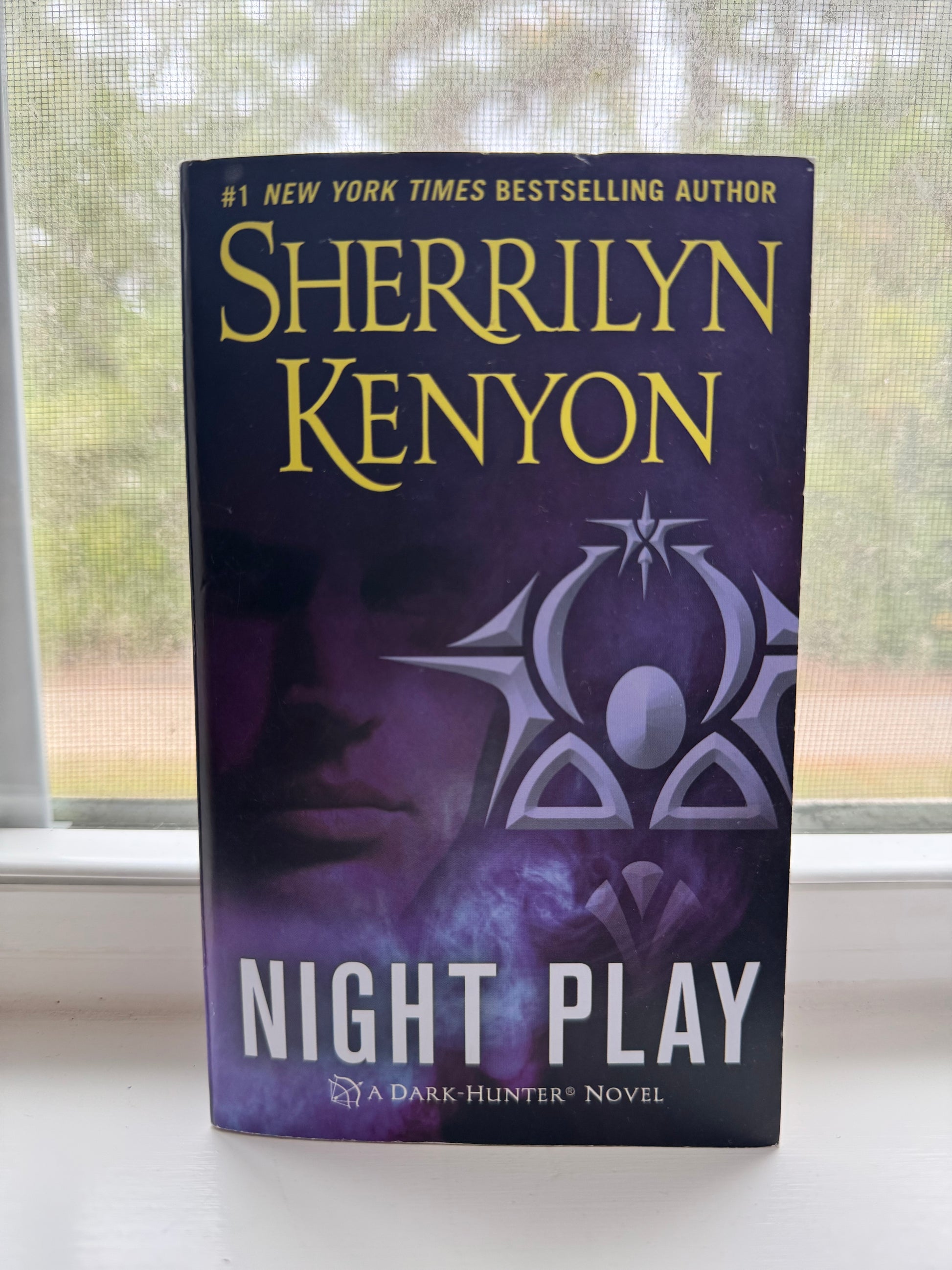 Book titled 'Night Play' by Sherrilyn Kenyon on a surface with a window in the background