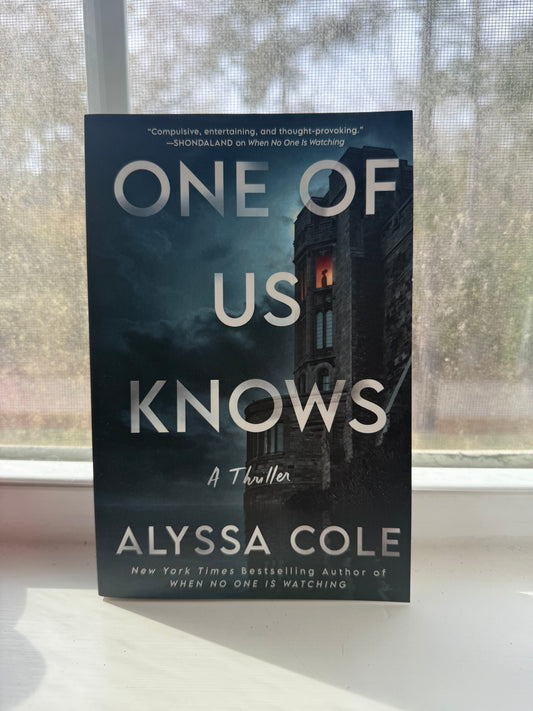 This image features the book cover of "One of Us Knows" by Alyssa Cole, a thriller novel. The cover displays a dramatic and dark image of a isolated house by the sea, with stormy clouds overhead, hinting at the thriller genre and the dramatic turn of events in the story.