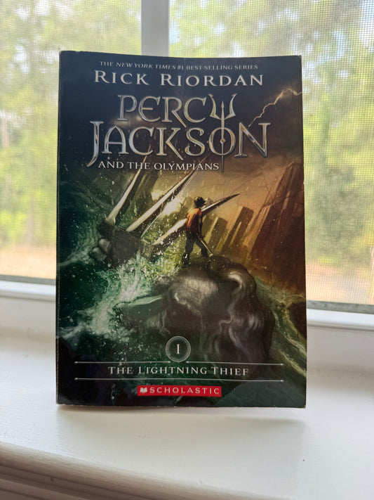 Book titled 'Percy Jackson and the Olympians' by Rick Riordan on a surface with a window in the background.