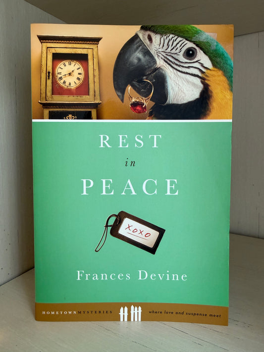 The book cover of 'Rest in Peace' by Frances Devine, featuring a mint green front cover with white text and a small black-and-white tag graphic, plus a top panel showing a clock and a blue-and-yellow parrot.