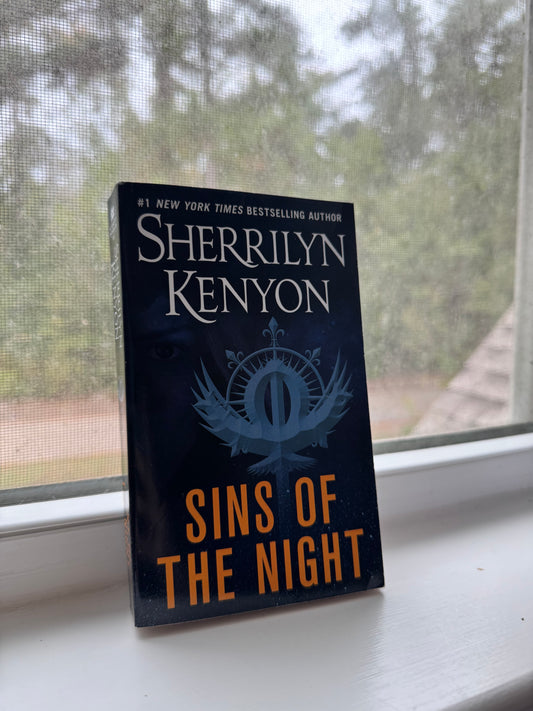Book titled 'Sins of the Night' by Sherrilyn Kenyon on a surface with a blurred outdoor background