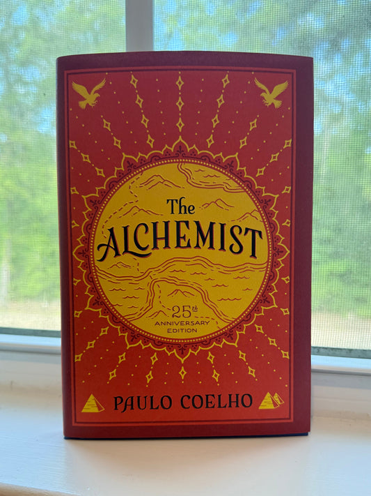 Book titled 'The Alchemist' by Paulo Coelho on a surface with a window in the background