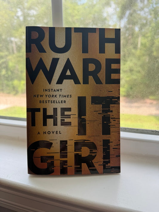 Book titled 'The Girl' by Ruth Ware on a surface with a window in the background